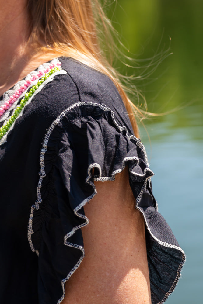 Detail of women’s flowy bohemian dress with deep V neckline and colorful handcrafted trim accents.