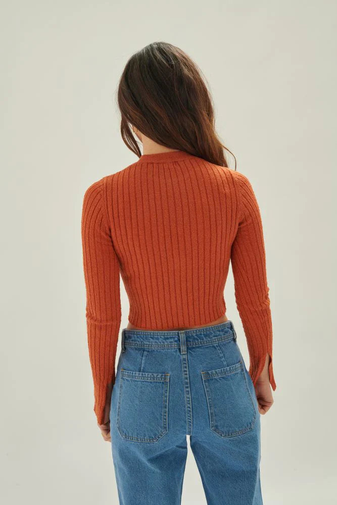 Fashion-forward burnt orange sweater with body-hugging fit and subtle flare cuffs for modern streetwear-inspired outfits.