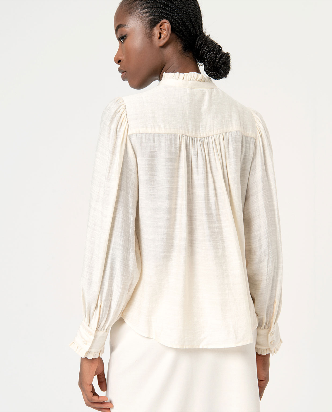 Back view, gathered, women’s flowy cream blouse with romantic ruffle details and effortless Parisian-inspired style aesthetic.