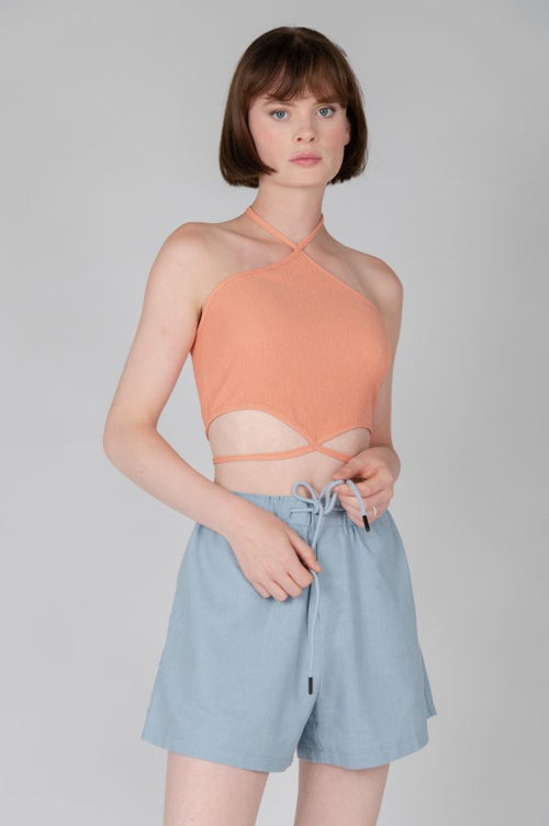 Peach ribbed halter crop top with crisscross neckline and cutout waist detail for women.