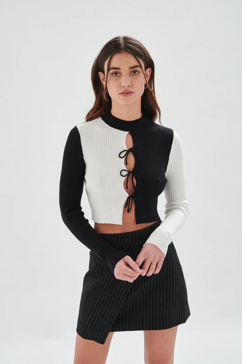Women’s two-tone black and white knit crop top with long sleeves and front tie accents for edgy Y2K-inspired fashion looks.