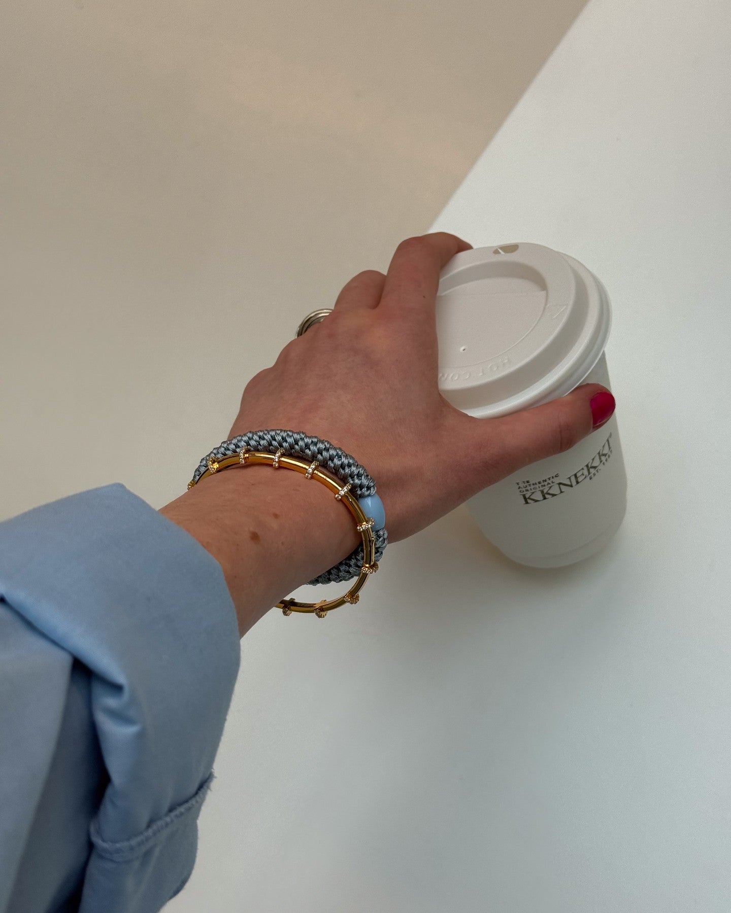 KKNEKKI Baby Blue.  Close up of a woman's wrist and hand holding a coffee cup, her bracelet looks great with a blue-silver Kknekki hair tie.