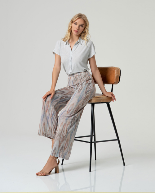 Chic woman sitting on a bar stool wearing a Lurex patterned pant against a white background