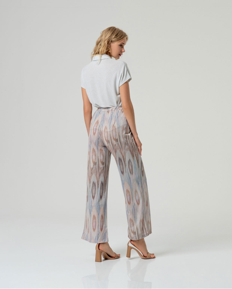 Back view of chic woman standing in a casual pose wearing a Lurex patterned pant and high-heeled sandals against a white background