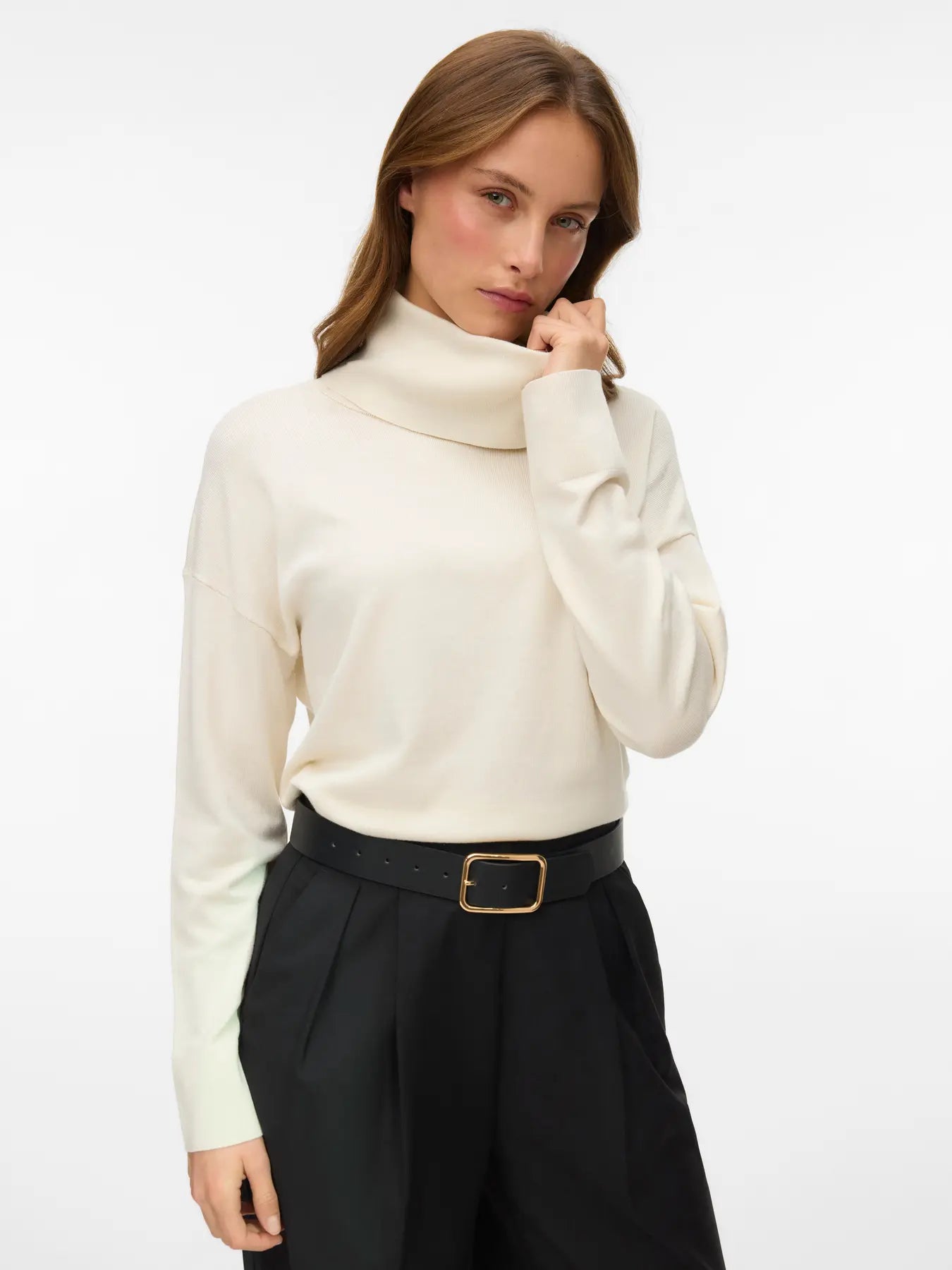 Women's birch colored turtleneck sweater with long sleeves and relaxed fit styled with tailored brown trousers.