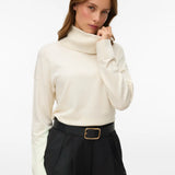Women's birch colored turtleneck sweater with long sleeves and relaxed fit styled with tailored brown trousers.