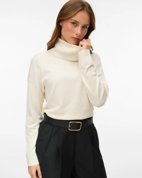 Women's birch colored turtleneck sweater with long sleeves and relaxed fit styled with tailored brown trousers.