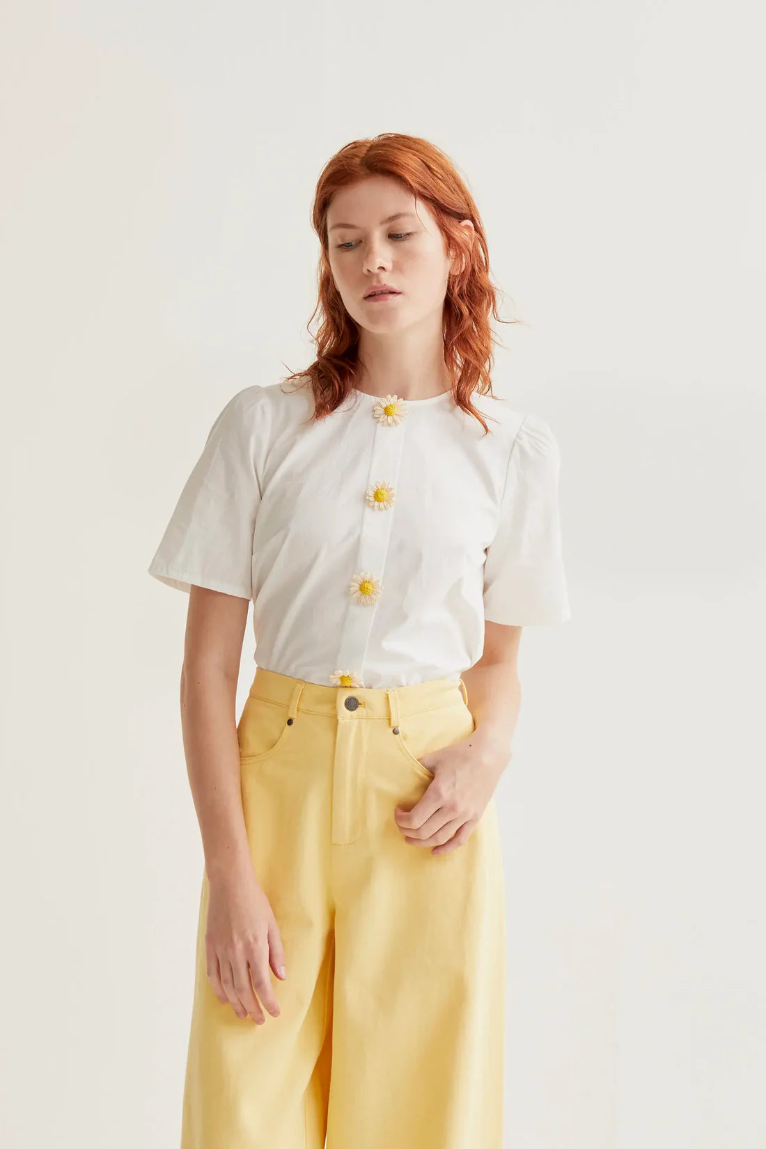Women's white short sleeve blouse with 3D daisy flower buttons, round neckline and subtle puff shoulders for feminine spring and summer style.
