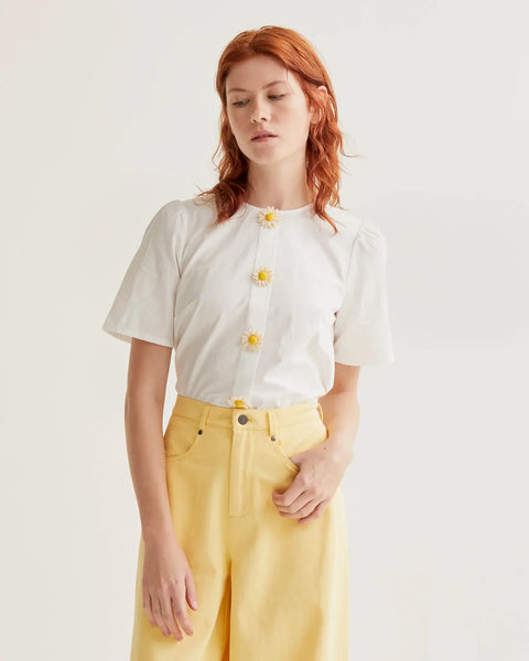 Women's white short sleeve blouse with 3D daisy flower buttons, round neckline and subtle puff shoulders for feminine spring and summer style.
