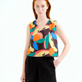 Young woman wearing a sleeveless top with colorful fruit pattern and black shorts on a white background.  Summer sporty.