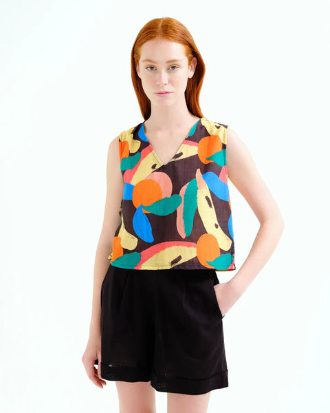 Young woman wearing a sleeveless top with colorful fruit pattern and black shorts on a white background.  Summer sporty.