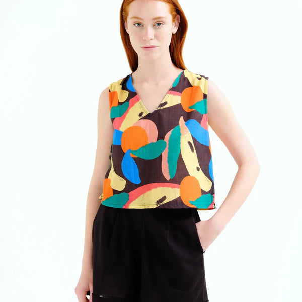 Young woman wearing a sleeveless top with colorful fruit pattern and black shorts on a white background.  Summer sporty.