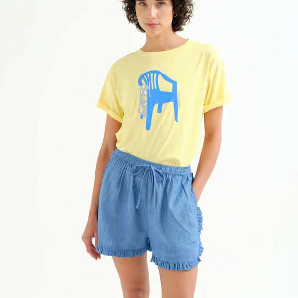 Women's pastel yellow graphic T-shirt featuring a bold blue chair illustration, rolled sleeves, crew neckline, and relaxed fit for casual everyday style.