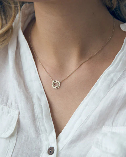 Minimalist gold dreamcatcher pendant necklace styled with a white linen blouse for effortless elegance.