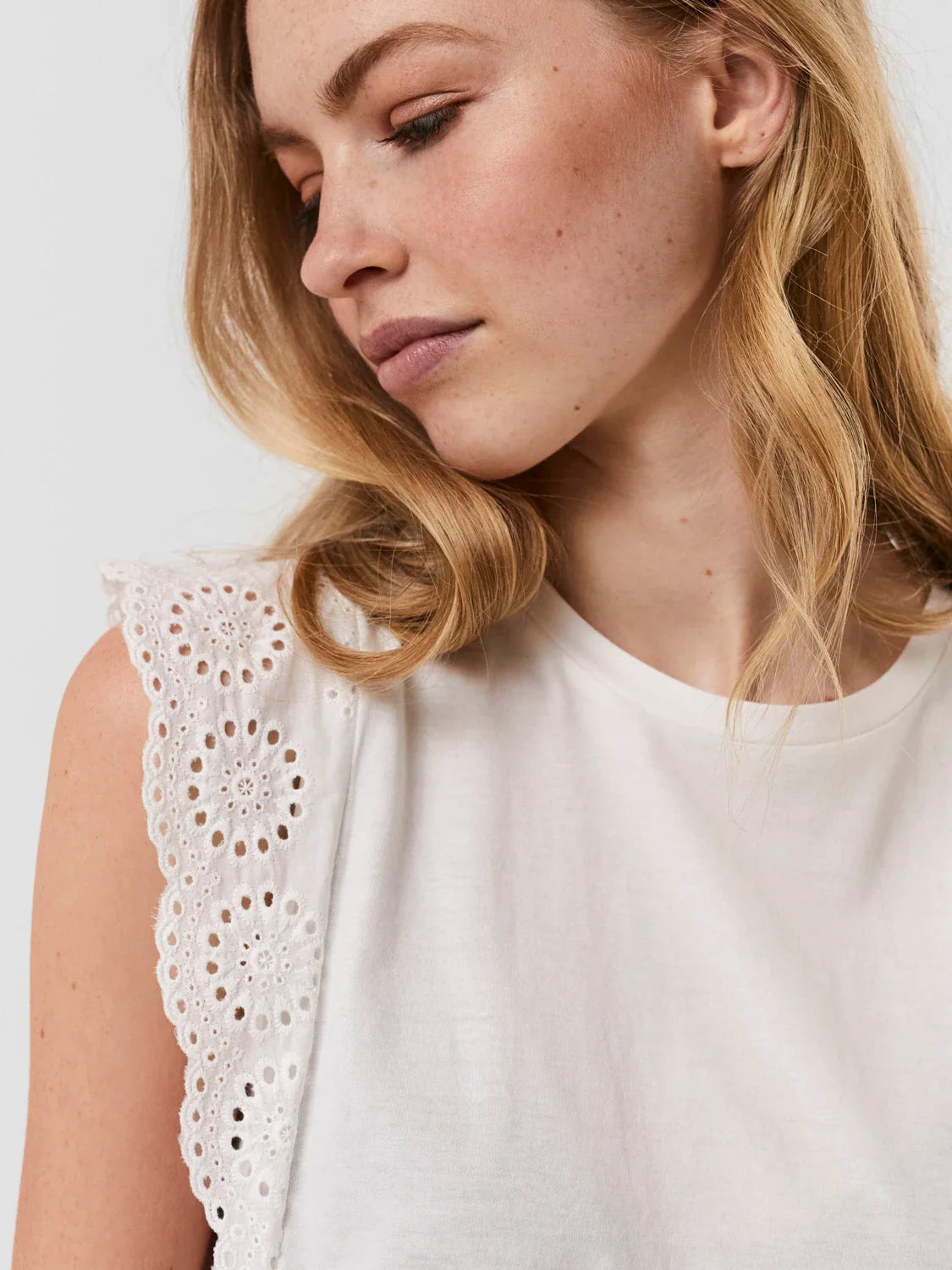 Women's white eyelet lace top featuring delicate embroidery and sleeveless silhouette.