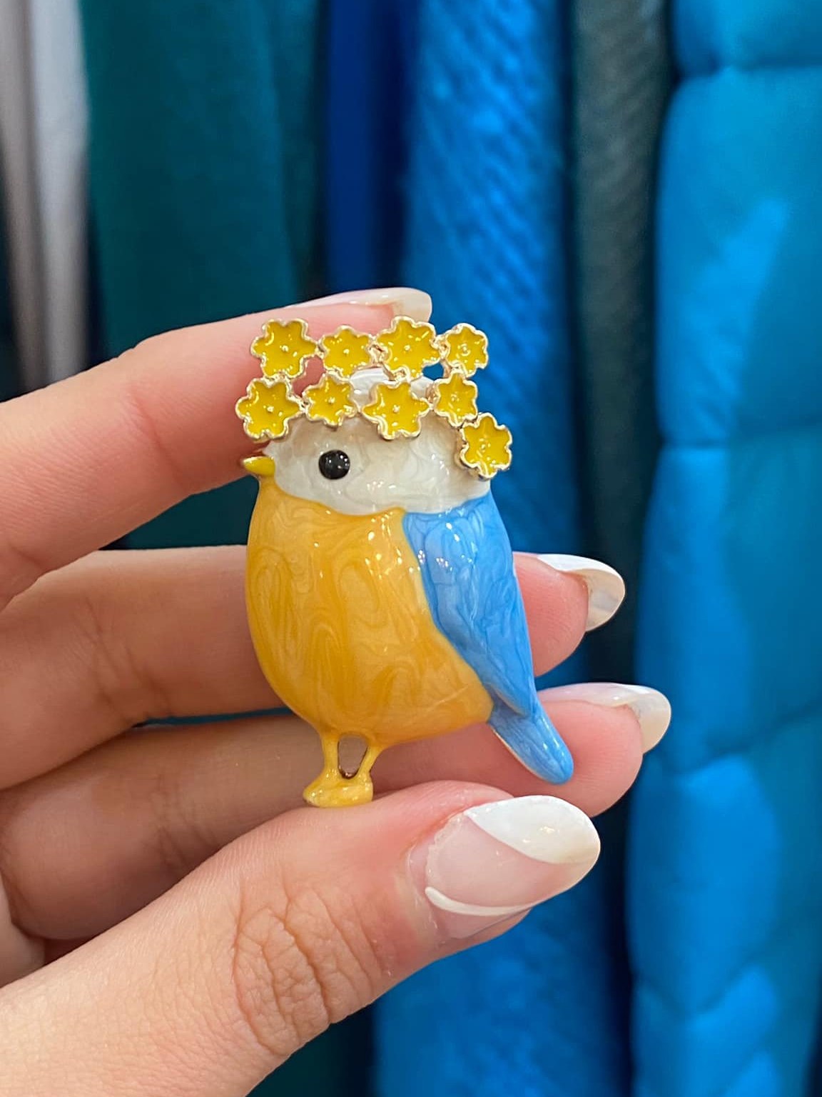 Cute spring-inspired bird pin featuring floral details and glossy enamel finish.