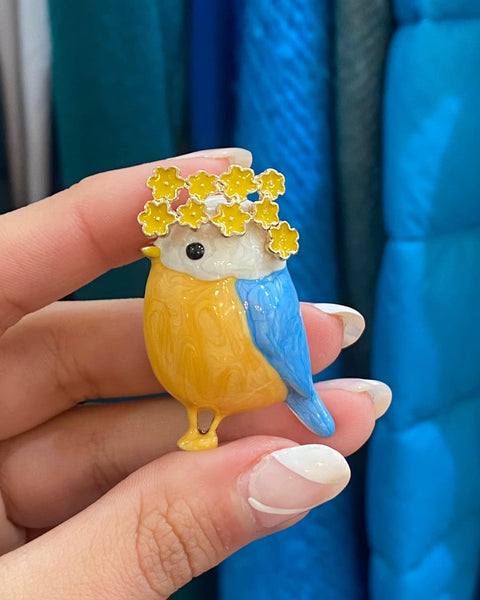 Cute spring-inspired bird pin featuring floral details and glossy enamel finish.