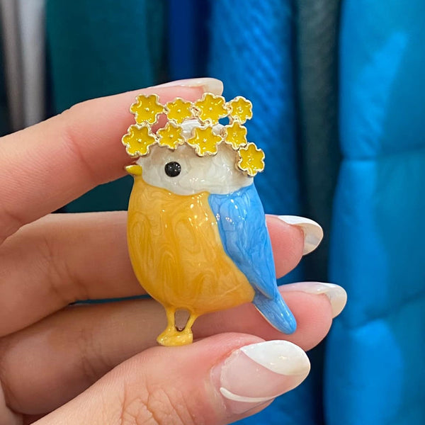 Cute spring-inspired bird pin featuring floral details and glossy enamel finish.