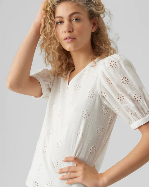 Feminine white broderie anglaise top featuring floral cutout embroidery and relaxed silhouette.