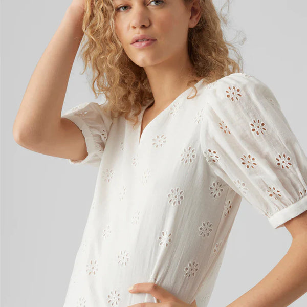 Feminine white broderie anglaise top featuring floral cutout embroidery and relaxed silhouette.