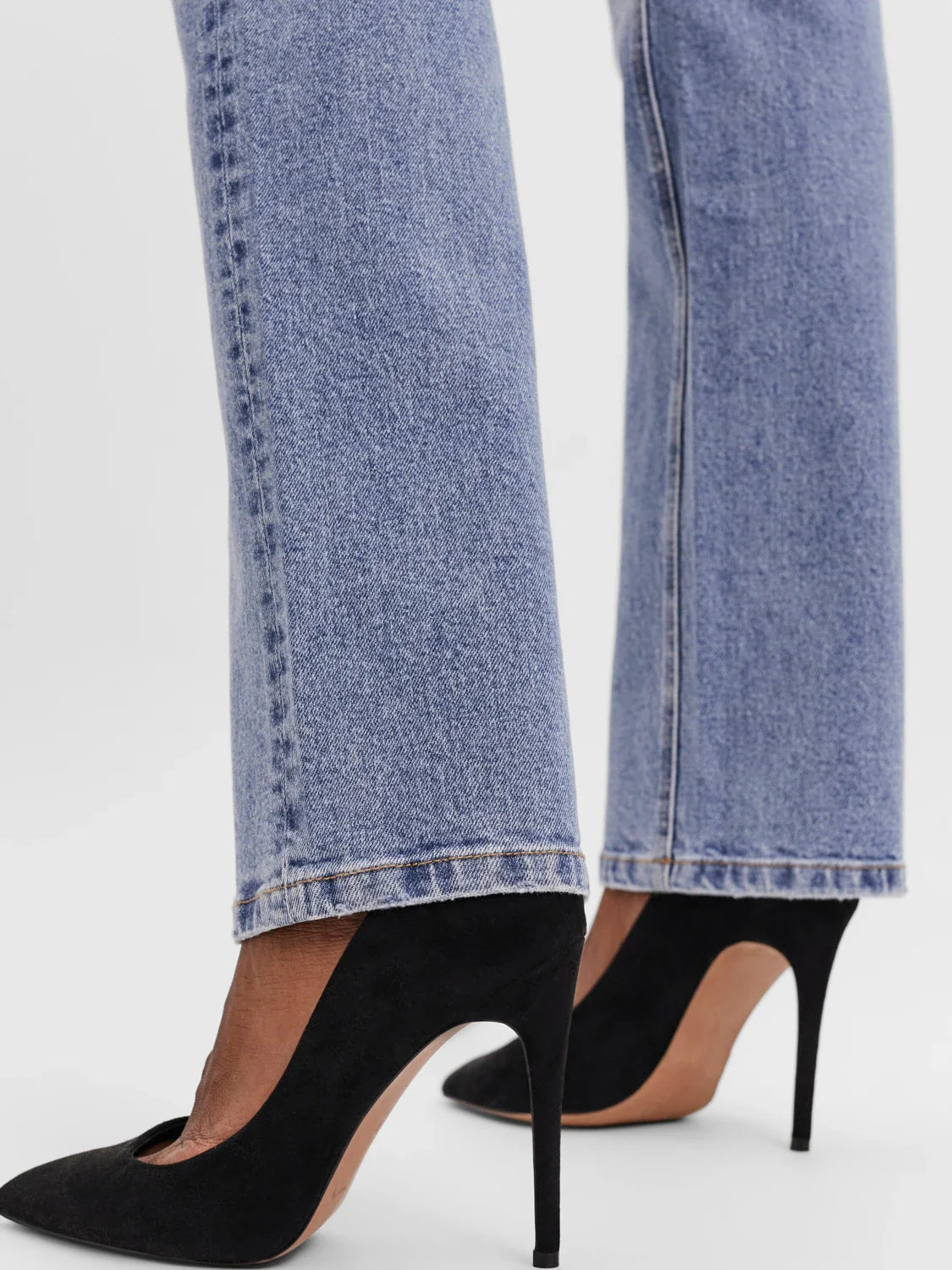 Detail of hem of minimalist straight leg jeans in light blue wash with flattering tailored fit for trendy capsule wardrobe fashion.