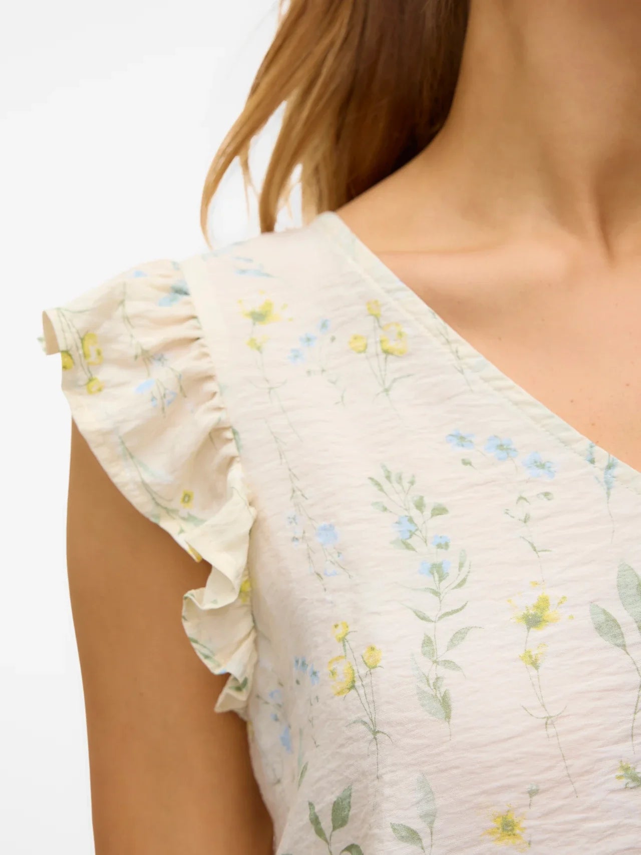 Detail of neckline and shoulders of soft ivory botanical print blouse with ruffled shoulders and effortless casual-luxe fashion appeal.