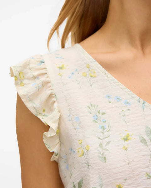 Detail of neckline and shoulders of soft ivory botanical print blouse with ruffled shoulders and effortless casual-luxe fashion appeal.