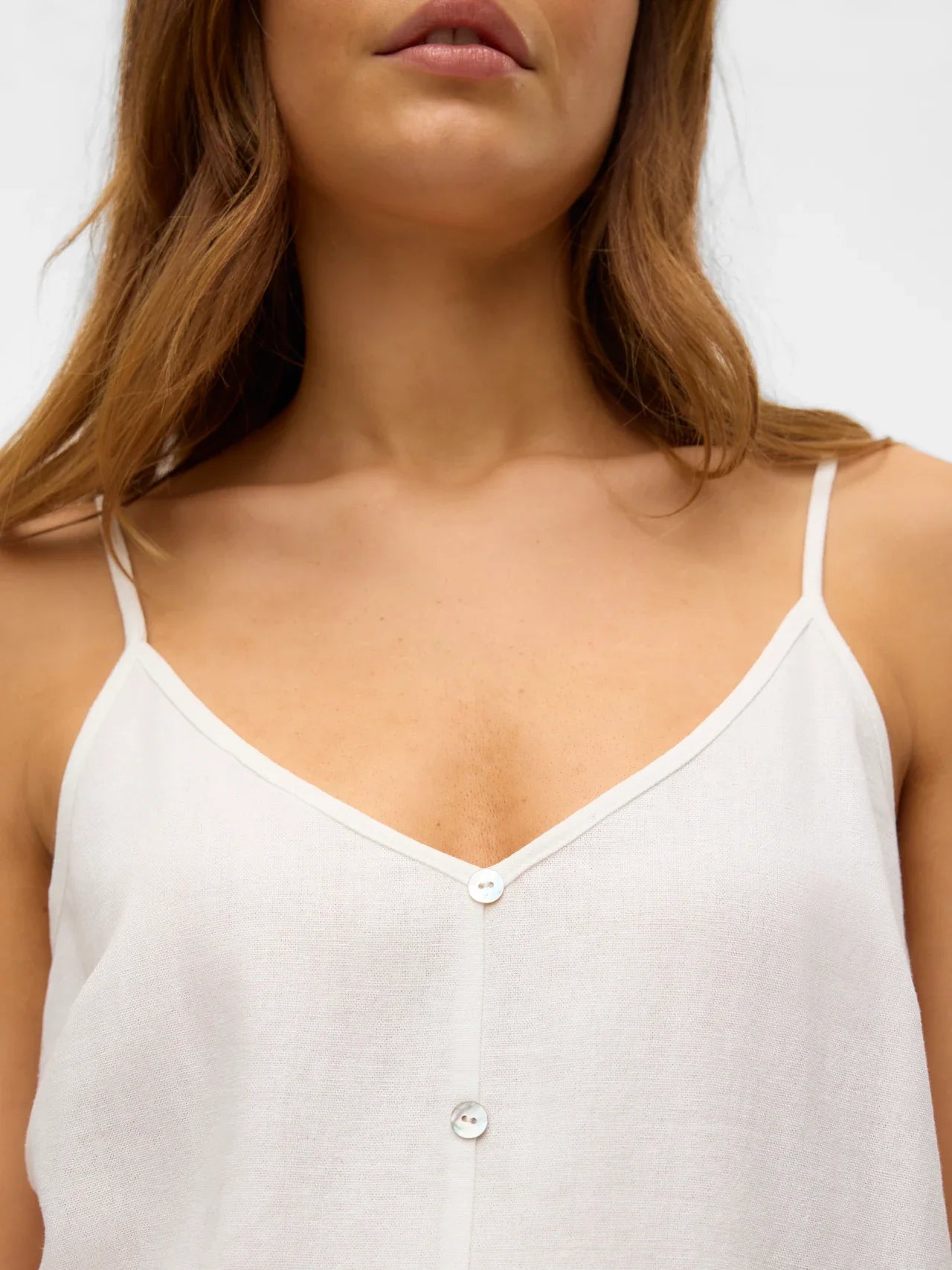 Women’s lightweight white cami top featuring front button accents and elegant minimalist resort-inspired styling.