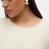 Detail of rolled neck of contemporary women’s beige knit top with understated luxury aesthetic and easy everyday layering style.